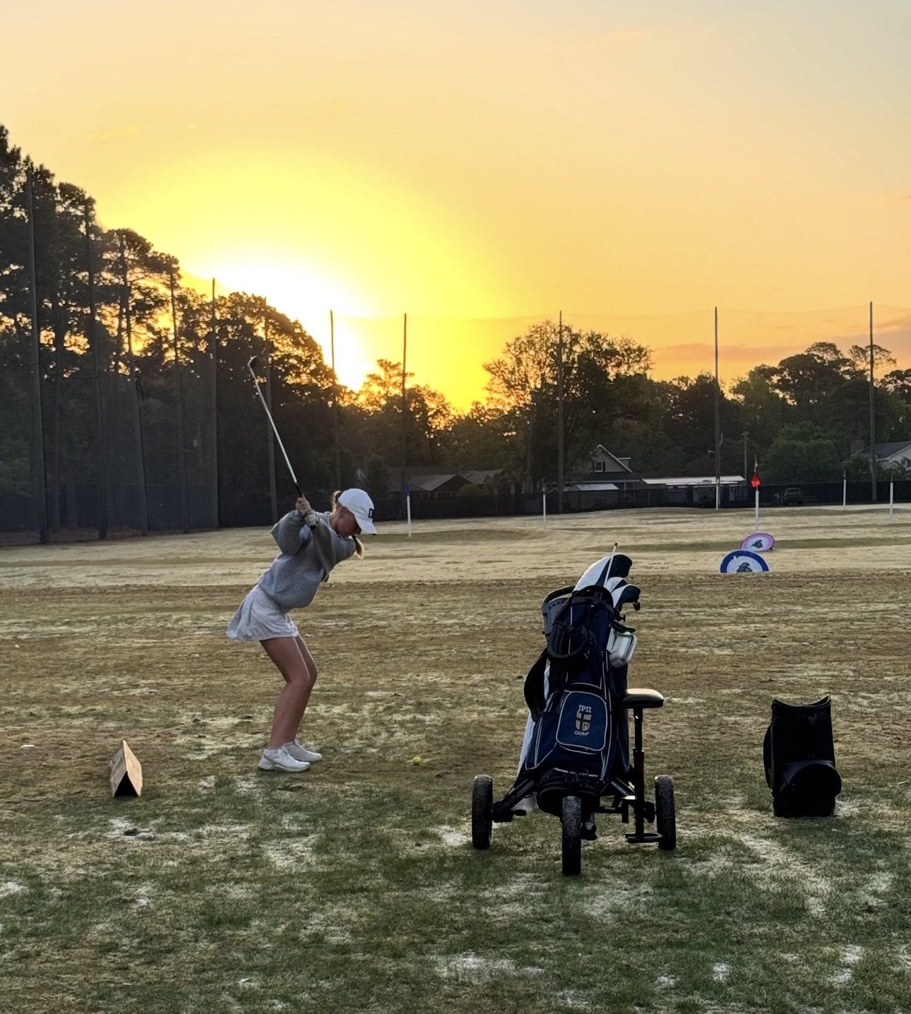 Sofie mid-backswing on the driving range at sunrise, golf bag beside her.